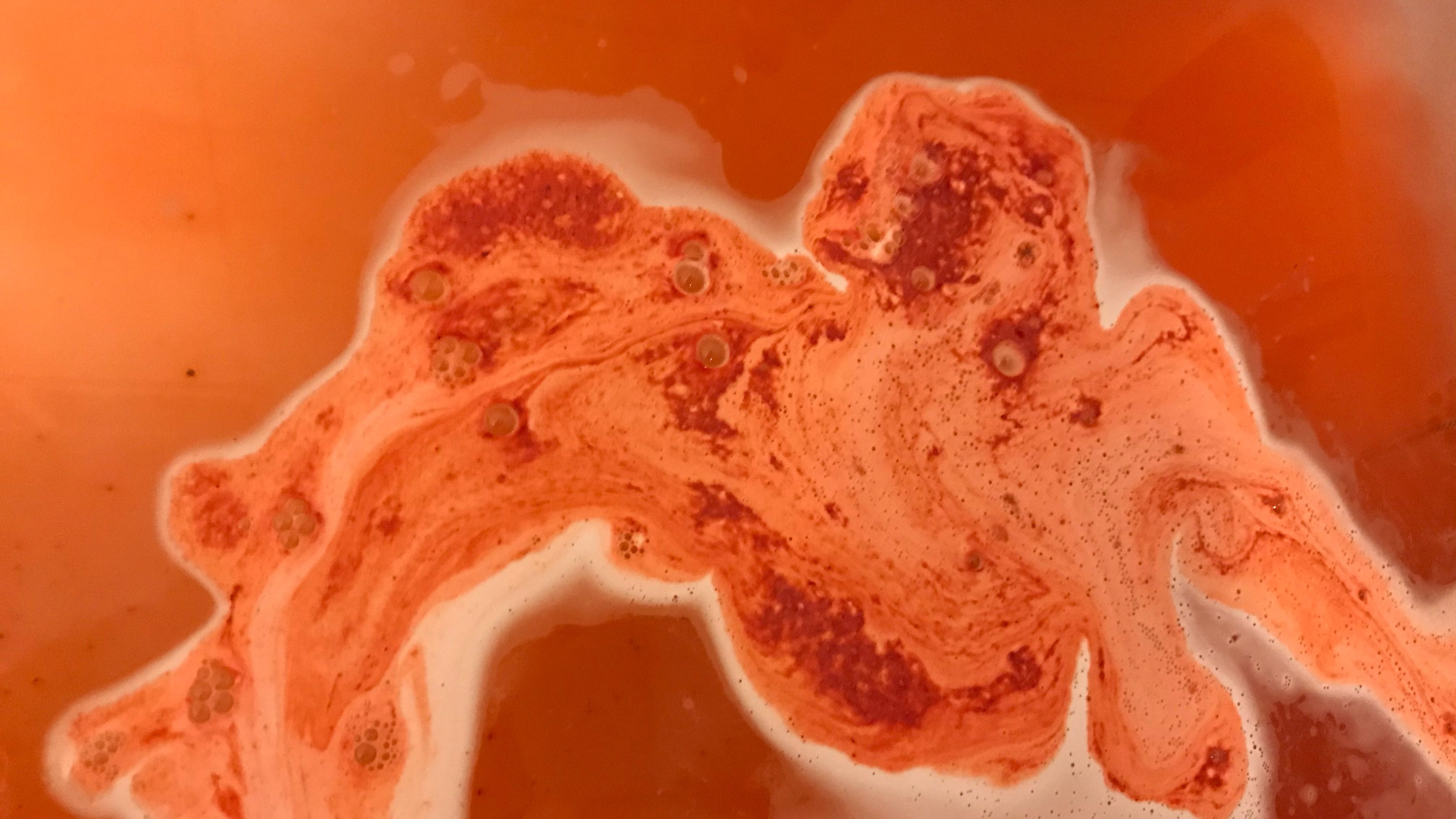 A photograph of my bath water, which has a red bath bomb mid fizz in it. The fizzing trail of the bath bomb looks disconcertingly organic.